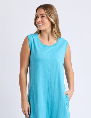 Woman wearing a sleeveless turquoise blue summer dress with side pocket details.