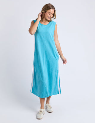 Woman wearing a sleeveless turquoise maxi dress with white side stripes and white sneakers.