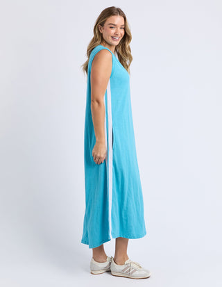 Woman wearing a turquoise sleeveless maxi dress with white side stripes and white sneakers.