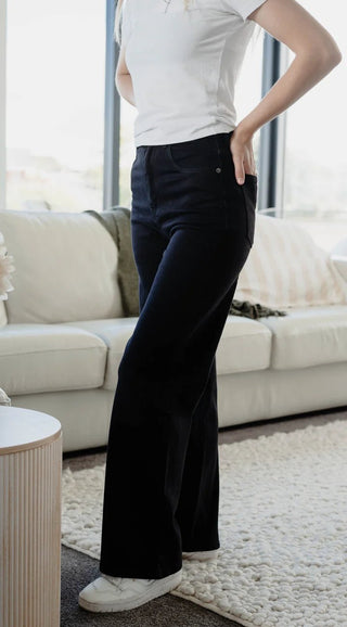 Woman wearing black high-waisted wide leg pants and a white t-shirt in a bright living room.