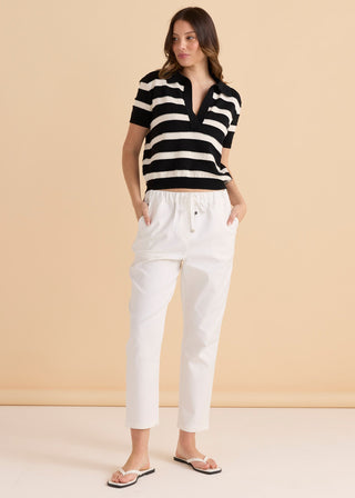 Woman wearing a black and white striped short sleeve polo and white trousers.