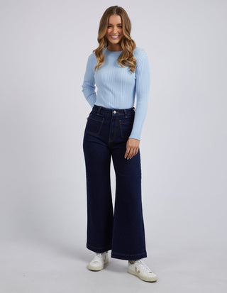 Woman wearing a light blue ribbed long sleeve top and dark wash wide leg jeans with white sneakers