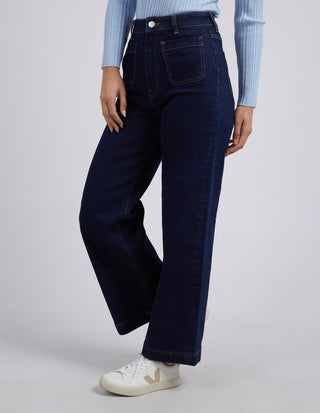 Woman wearing dark blue wide-leg denim jeans, a light blue ribbed top, and white sneakers.