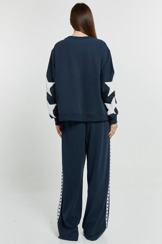 Woman wearing navy blue oversized sweatshirt with white star sleeves and matching wide-leg joggers.
