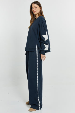 Woman wearing navy blue oversized sweatshirt with white star sleeves and matching wide-leg joggers.