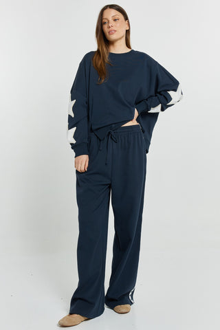 Woman wearing navy blue oversized sweatshirt with white star detail and matching wide-leg joggers