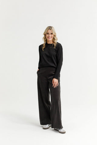 Woman wearing a black long-sleeve top and wide-leg black lounge pants with sneakers.