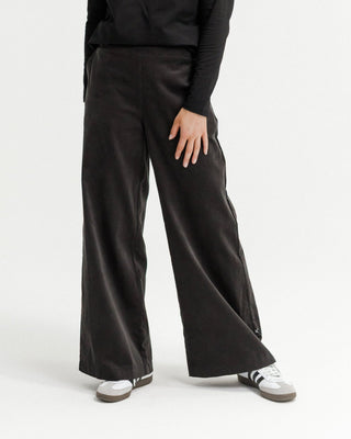 Woman wearing black wide-leg lounge pants and white sneakers against a white background.