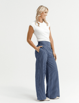Woman wearing white sleeveless top and blue and white striped wide leg pants