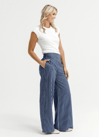 Woman wearing white sleeveless top and blue vertical striped wide leg pants.