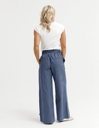 Woman wearing white t-shirt and blue vertical striped wide-leg trousers.