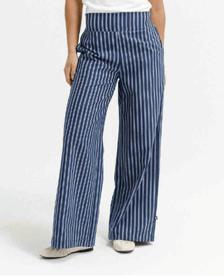 Woman wearing navy blue and white striped wide-leg trousers and beige flat shoes.