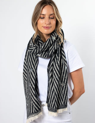 Woman wearing a black and white chevron pattern scarf with star details and fringe edges.