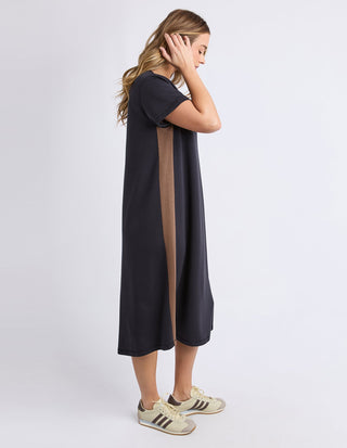 Woman wearing a navy blue midi dress with a brown side stripe and beige sneakers