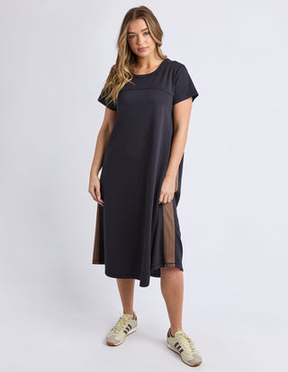 Woman wearing a navy blue short-sleeve midi dress with brown side panel accents and sneakers.