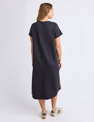 Rear view of a woman wearing a black short-sleeve midi dress and beige sneakers.