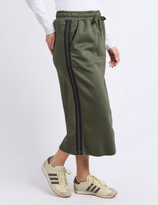 Woman wearing olive green athletic maxi skirt with black side stripes and beige sneakers