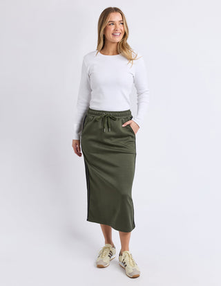 Woman wearing a white long sleeve t-shirt and olive green maxi skirt with sneakers.