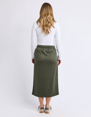 Rear view of a woman wearing a white long-sleeve top and olive green maxi skirt.