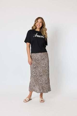 Woman wearing a black graphic t-shirt and leopard print maxi skirt with beige sandals.