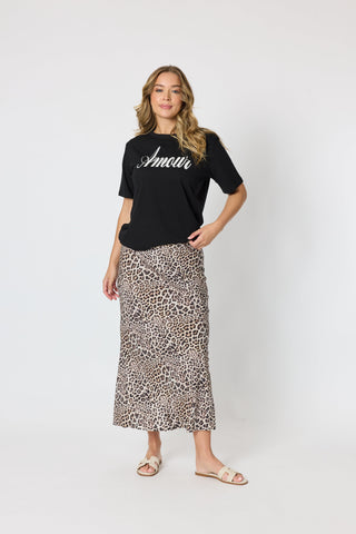Woman wearing a black Amour graphic t-shirt and a leopard print midi skirt with sandals.