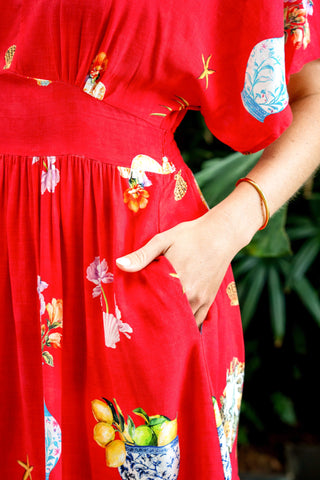 Woman wearing a red floral print summer dress with pockets and a gold bracelet.