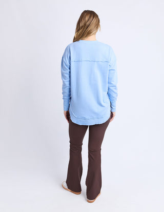 Woman wearing a light blue long sleeve sweatshirt and brown flared trousers.