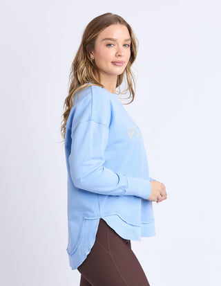 Woman wearing a light blue Foxwood sweatshirt and brown leggings.