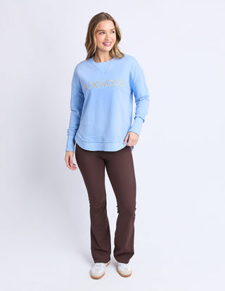 Woman wearing a light blue Foxwood sweatshirt and brown flared pants.