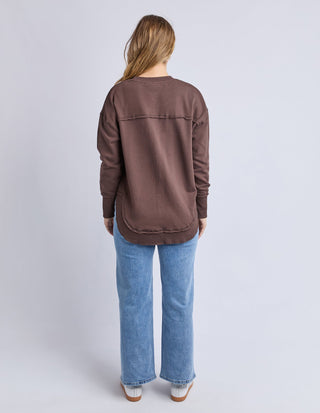 Woman wearing a brown oversized sweatshirt and light wash blue wide-leg jeans.
