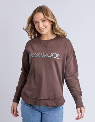 Woman wearing a brown Foxwood sweatshirt and blue jeans.