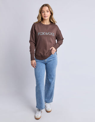 Woman wearing a brown Foxwood sweatshirt and light blue wide-leg denim jeans.