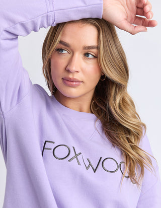 Woman wearing a lilac Foxwood sweatshirt with graphic text logo.