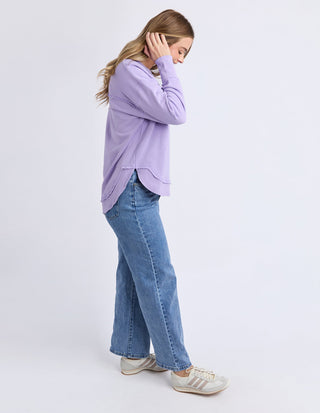 Woman wearing a lilac sweatshirt and blue wide-leg denim jeans with white sneakers.