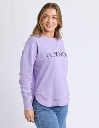 Woman wearing a lilac Foxwood sweatshirt and blue jeans.