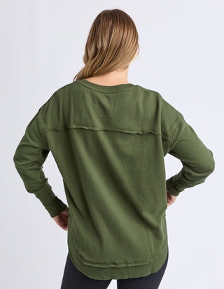 Rear view of a woman wearing an olive green long sleeve sweatshirt with a raw edge seam detail.