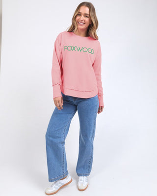 Woman wearing a pink Foxwood sweatshirt and blue wide-leg denim jeans.