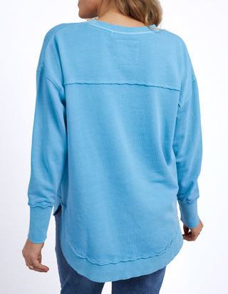 Back view of a woman wearing a light blue long sleeve sweatshirt and denim jeans.