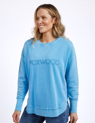 Woman wearing a blue Foxwood sweatshirt and denim jeans.
