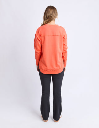 Back view of a woman wearing a coral orange long-sleeve sweatshirt and black flared pants.