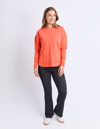 Woman wearing an orange Foxwood sweatshirt and black flare pants with white sneakers.