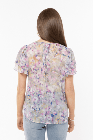Woman wearing a floral print short sleeve blouse with ruffled sleeves and light blue jeans.