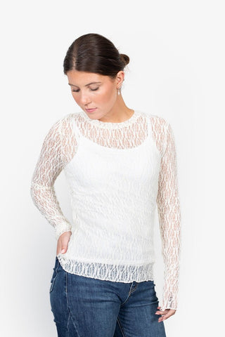 Woman wearing a white long sleeve lace overlay top with a camisole underneath and blue jeans.