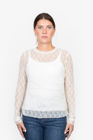 Woman wearing a white long-sleeve lace overlay top with a white camisole and blue jeans.