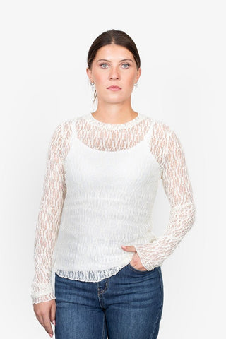 Woman wearing a white long-sleeve lace top over a white camisole and blue denim jeans.