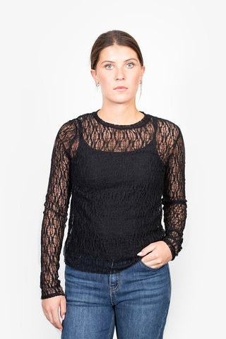 Woman wearing a black lace long sleeve top over a black camisole and blue jeans.