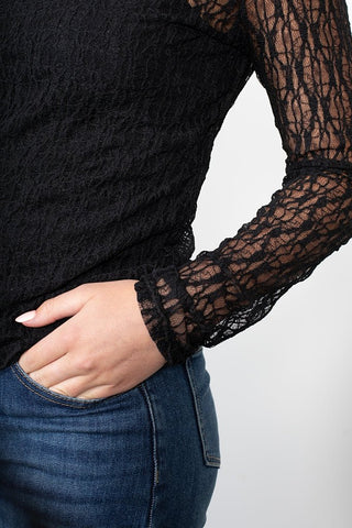 Woman wearing a black long sleeve lace top and blue denim jeans.