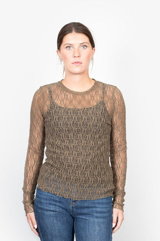Woman wearing a brown long-sleeved lace mesh top and blue jeans.