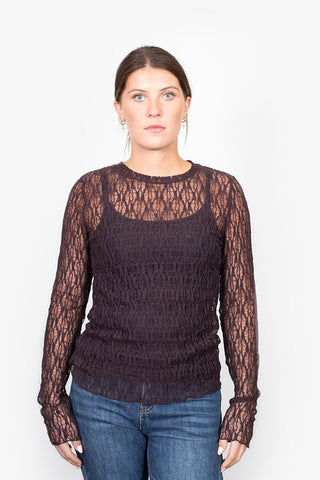 Woman wearing a long sleeve dark purple lace sheer top with blue jeans