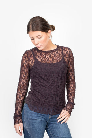 Woman wearing a dark purple long sleeve lace top and blue denim jeans.